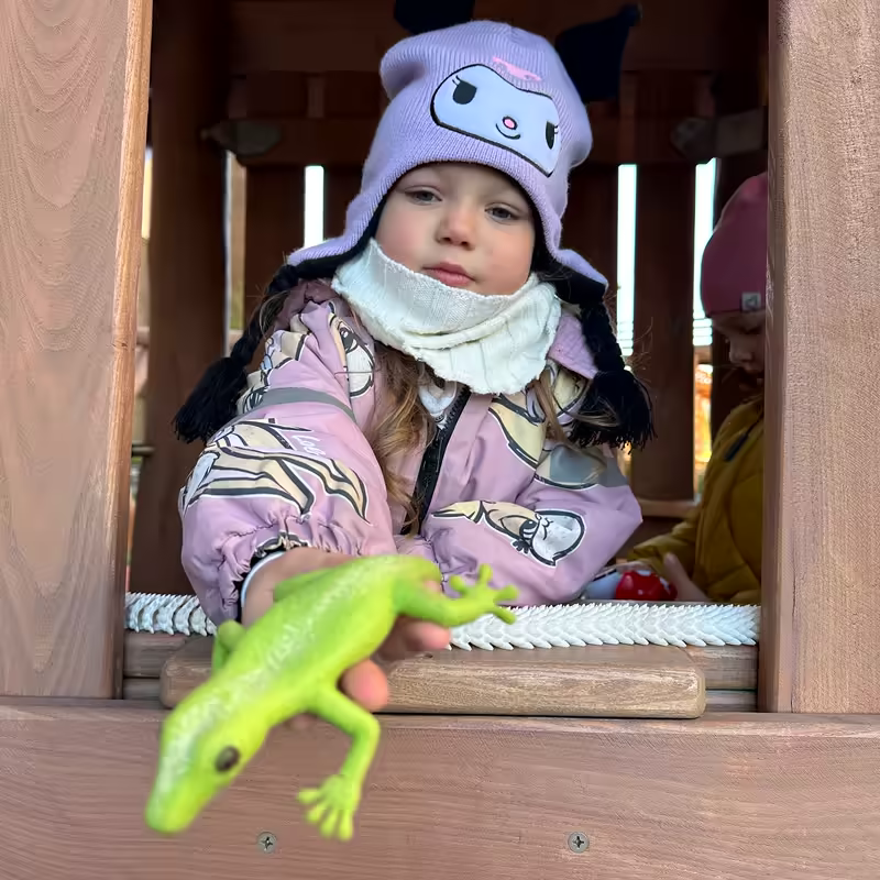 Девочка в игровом домике, на перилах игрушечная ящерица